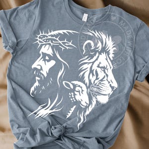 Puede incluir: Camiseta azul claro con un diseño gráfico blanco. El diseño incluye el perfil de una persona con una corona de espinas, un león y un cordero. La camiseta tiene cuello redondo y mangas cortas.