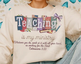 May include: Cream-colored sweatshirt with the words "Teaching is my ministry" in a patchwork design. The text includes the Bible verse Colossians 3:23. A pencil and bow are also featured in the design. The sweatshirt has long sleeves.