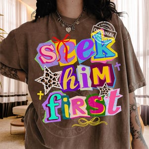Può includere: T-shirt marrone con la scritta "Seek Him First" in lettere a blocchi colorate. Il design include stelle con stampa leopardata e un fiocco. La maglietta ha un aspetto vintage e scollo tondo.