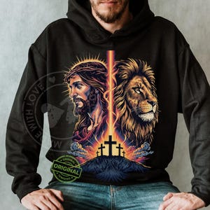 May include: Black hoodie featuring a graphic of Jesus Christ and a lion, with a cross and a beam of light. The design includes the text "ORIGINAL" and "WITH LOVE".