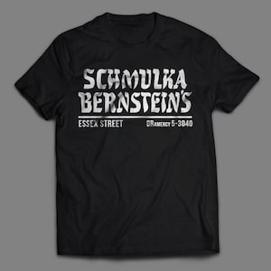 May include: Black t-shirt with white text that reads "Schmulka Bernstein's Essex Street Gramercy 5-3040"