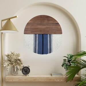 Puede incluir: Un tapiz de pared redondo con una mitad superior de madera y una mitad inferior tejida de blanco y azul. La parte superior de madera es de color marrón oscuro y la parte inferior tejida tiene rayas blancas y azules.