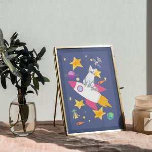 May include: A framed illustration of a cat riding a rocket through space. The rocket is white with pink and yellow accents. The cat is gray and white with a pink nose. The background is dark blue with stars, planets, and a satellite.