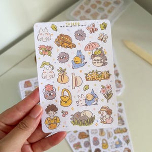 Puede incluir: Una hoja de pegatinas con varios personajes de dibujos animados y dise&ntilde;os florales. Las pegatinas incluyen im&aacute;genes de animales, flores y otros elementos caprichosos. El texto "TOTORO FROTHY LATTE STUDIO" est&aacute; impreso en la parte superior de la hoja.