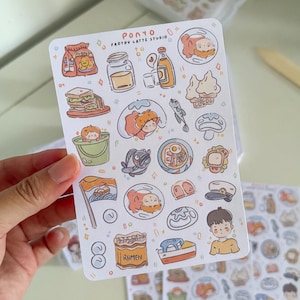 Puede incluir: Una hoja de pegatinas con ilustraciones de comida de estilo caricatura, incluyendo ramen, s&aacute;ndwiches y pescado. Las pegatinas son de colores suaves y tienen el texto "Ponyo Frothy Latte Studio".