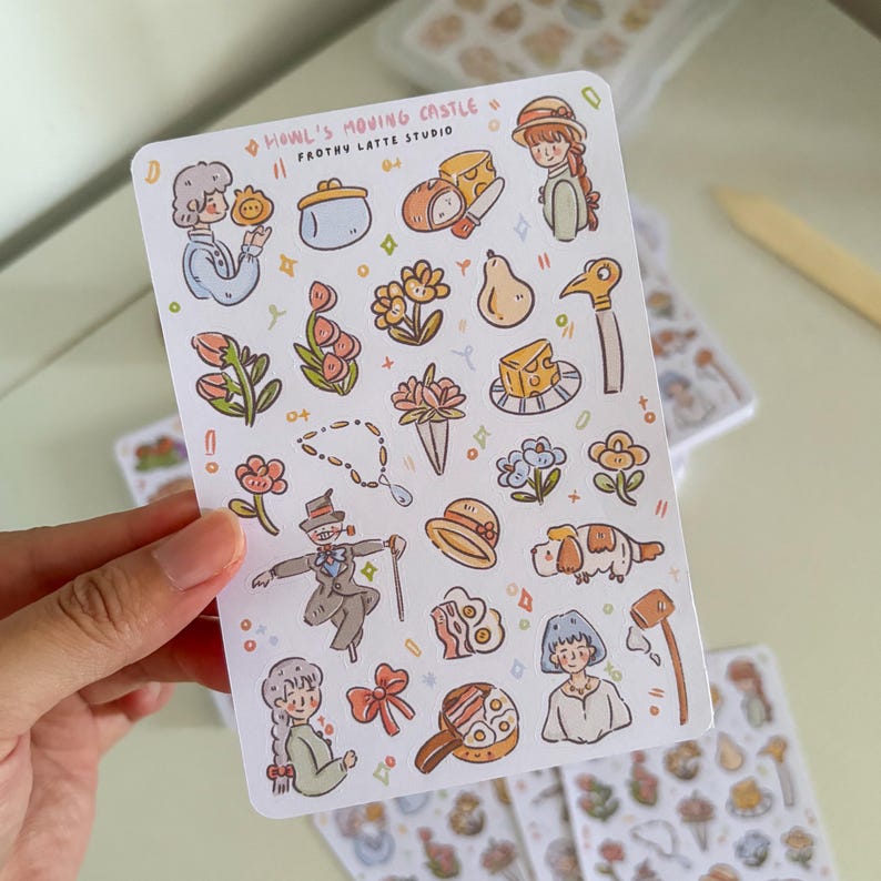 Puede incluir: Una hoja de pegatinas con ilustraciones de "El castillo ambulante". Las pegatinas representan personajes, alimentos y accesorios con un estilo caprichoso. El texto "HOWL'S MOVING CASTLE" y "FROTHY LATTE STUDIO" es visible.