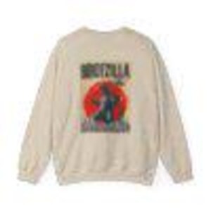 Puede incluir: Sudadera de color crema con un gr&aacute;fico de Godzilla en silueta contra un c&iacute;rculo rojo, con el texto "GODZILLA" arriba y "DESTROY ALL MONSTERS" abajo. El dise&ntilde;o est&aacute; impreso en negro y rojo.