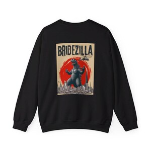 Puede incluir: Sudadera negra con un gr&aacute;fico de estilo vintage de un monstruo similar a Godzilla con la etiqueta "Bridezilla". El dise&ntilde;o incluye un sol rojo, un horizonte urbano y un helic&oacute;ptero. La sudadera est&aacute; hecha de un material suave.