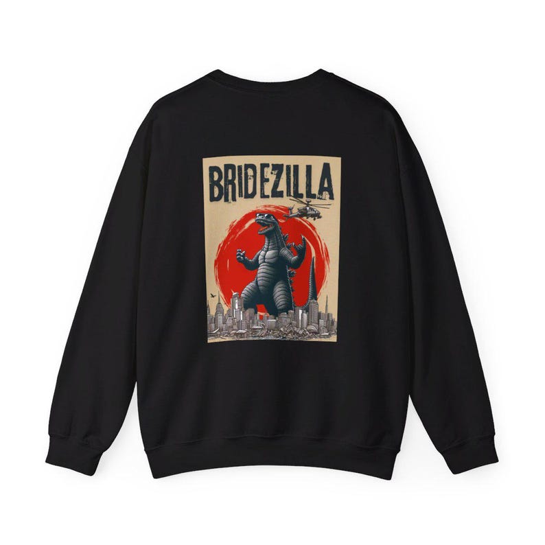 Puede incluir: Sudadera negra con un gr&aacute;fico de estilo vintage de un monstruo similar a Godzilla con la etiqueta "Bridezilla". El dise&ntilde;o incluye un sol rojo, un horizonte urbano y un helic&oacute;ptero. La sudadera est&aacute; hecha de un material suave.
