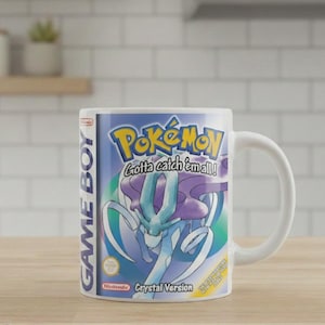 以下が含まれることがあります： 任天堂ゲームボーイ用ソフト「ポケットモンスター クリスタルバージョン」のパッケージアートがプリントされた白いセラミック製マグカップ。ポケモンロゴ、Gotta catch em all!の文字、ゲームボーイのロゴ、スイクンのキャラクターが描かれています。