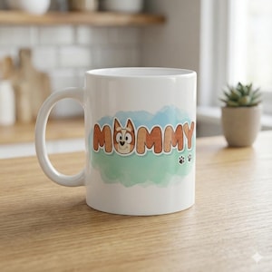 May include: White ceramic mug featuring the word "MOMMY" in brown letters with a cartoon dog face incorporated into the letter "O". The design includes a blue and green watercolor background and paw prints.