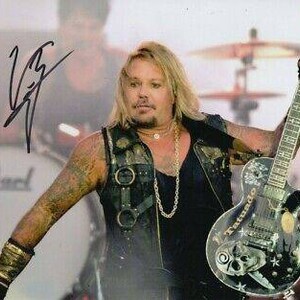 May include: A black and white electric guitar with a skull design and the text "Tornado" on the body. The guitar is being held by a person wearing a black vest with a silver chain necklace.