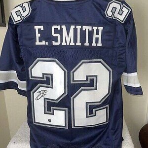 May include: A navy blue football jersey with the number 22 and the name "E. SMITH" on the back. The jersey is signed in silver marker.