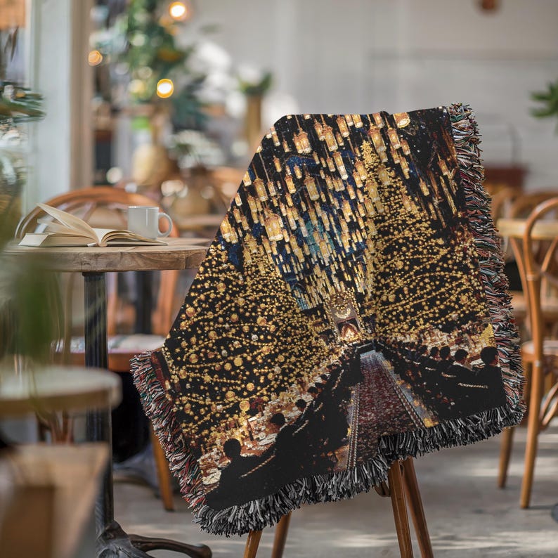 May include: A decorative throw blanket with a detailed image of a nighttime scene with golden lights and a pathway. The blanket is draped over a wooden chair. The edges have a fringed trim in shades of red, black, and brown.