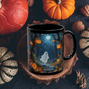 May include: Black ceramic mug featuring a Halloween-themed illustration. The design depicts a spooky forest scene with a ghost, jack-o'-lanterns, and a full moon. The mug is surrounded by pumpkins and gourds, perfect for the fall season.