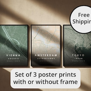 Può includere: Set di tre stampe incorniciate di mappe di città, con Vienna, Amsterdam e Tokyo. Ogni stampa ha una cornice nera e una palette di colori neutri. Il testo "Set of 3 poster prints with or without frame" è visualizzato sotto.