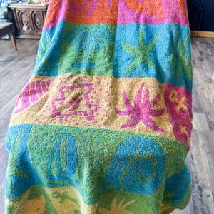 May include: A colorful beach towel draped over a chair. The towel features horizontal stripes of orange, pink, green, blue, and yellow, with palm tree and starfish designs. The towel is made of a soft, absorbent material.