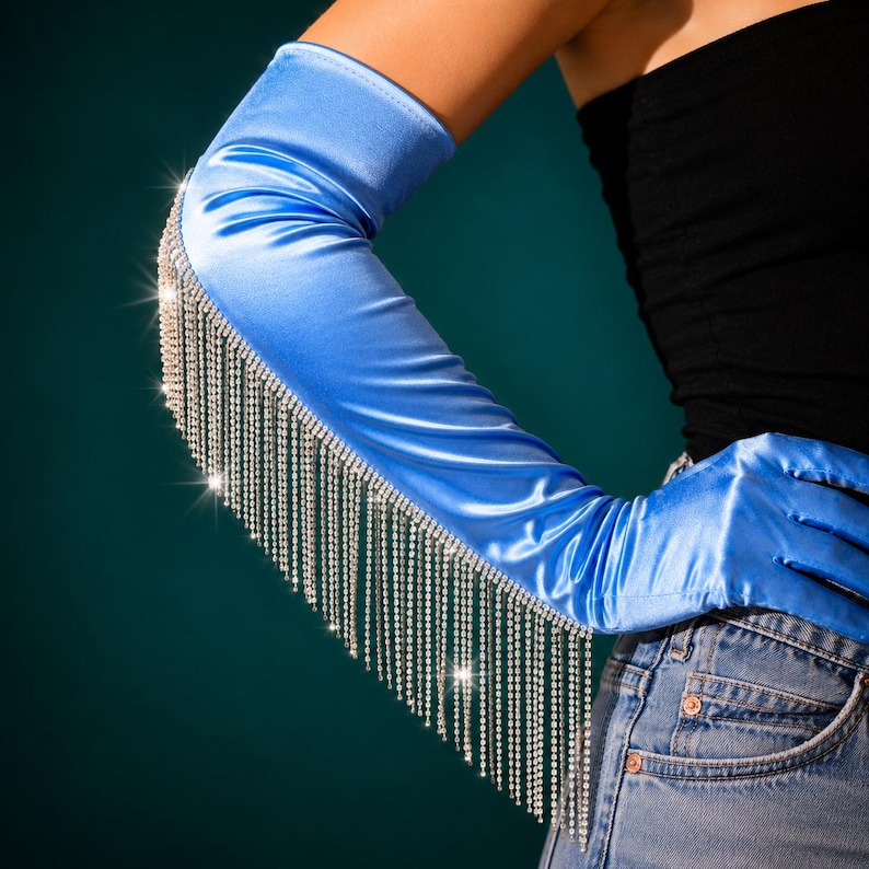 May include: A bright blue satin opera-length glove featuring a long fringe of sparkling clear rhinestones attached along the outer arm. The smooth, lustrous fabric extends from the fingers up to the upper arm, accented by dangling crystal chains.
