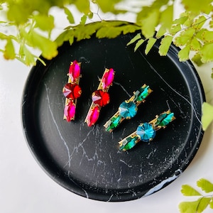 Puede incluir: Cinco pinzas para el pelo con pedrería de colores. Dos pinzas tienen pedrería roja y tres pinzas tienen pedrería azul y verde.