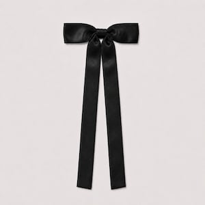 May include: A black satin bow accessory featuring a central knot and two long, straight, vertical ribbon tails extending downward. The fabric has a smooth, reflective sheen, and the overall design is symmetrical with clean, sharp edges throughout.