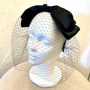 May include: A black satin bow headband with a black tulle veil attached. The headband is worn on a white mannequin head.
