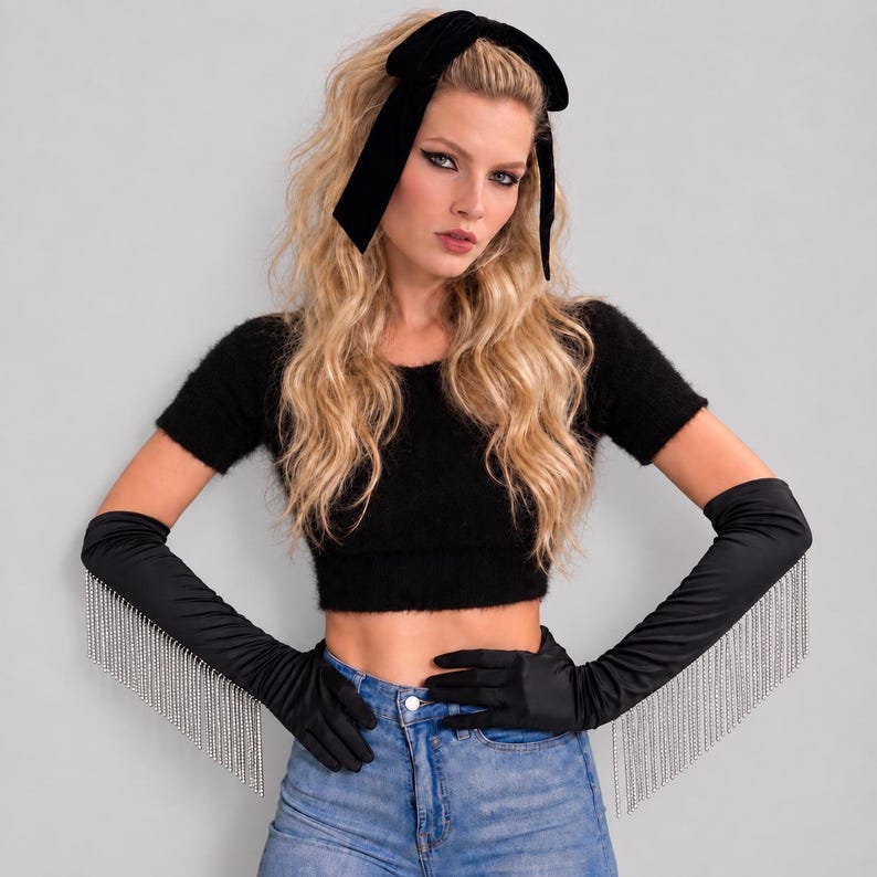 May include: Black opera-length satin gloves featuring long silver-toned crystal fringe trim along the outer forearms. The gloves are paired with a black fuzzy short-sleeve crop top and a black velvet hair bow headband.