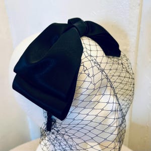 May include: A black satin bow headband with a black tulle veil. The headband is designed to be worn on the head with the bow sitting on top and the veil cascading down the back.