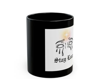Puede incluir: Taza de café negra con un diseño blanco que presenta una ilustración estilizada de una cara con los ojos cerrados y lágrimas. El texto "Stay Lost" está impreso debajo de la ilustración.