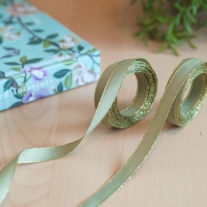 May include: Two spools of sage green ribbon with gold glitter trim. The ribbon is rolled up and the ends are tied together.