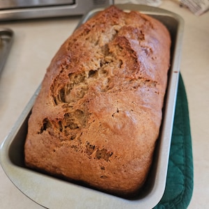 Könnte beinhalten: Ein Bananenbrot in einer silbernen Kastenform, das auf einem grünen Geschirrtuch liegt.