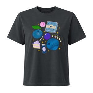 May include: A charcoal gray t-shirt featuring a graphic print of blueberries, a slice of blueberry cake, a jar, a carton labeled "BEST BERRY", and small yellow stars. The design includes various shades of blue, purple, and green elements.