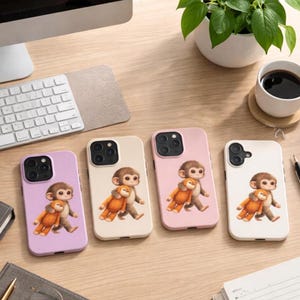 May include: Four phone cases in different colors: lavender, cream, pink, and white. Each case features a cartoon monkey hugging a teddy bear. The cases are on a wooden desk with a keyboard, coffee cup, and plant in the background.