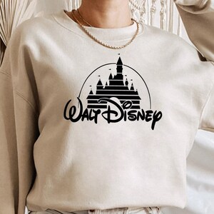 May include: A beige sweatshirt with a black graphic of the Walt Disney World castle and the text "Walt Disney" in a stylized font.
