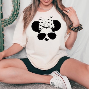 May include: A white t-shirt with a black and white illustration of Minnie Mouse wearing sunglasses. Minnie Mouse has a black bow with white polka dots.
