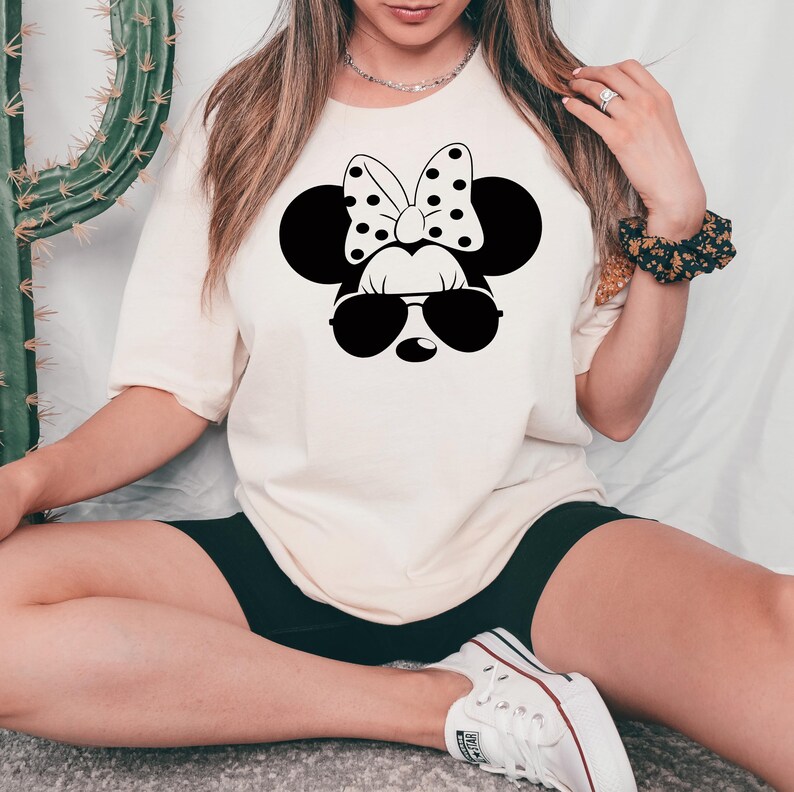May include: A white t-shirt with a black and white illustration of Minnie Mouse wearing sunglasses. Minnie Mouse has a black bow with white polka dots.