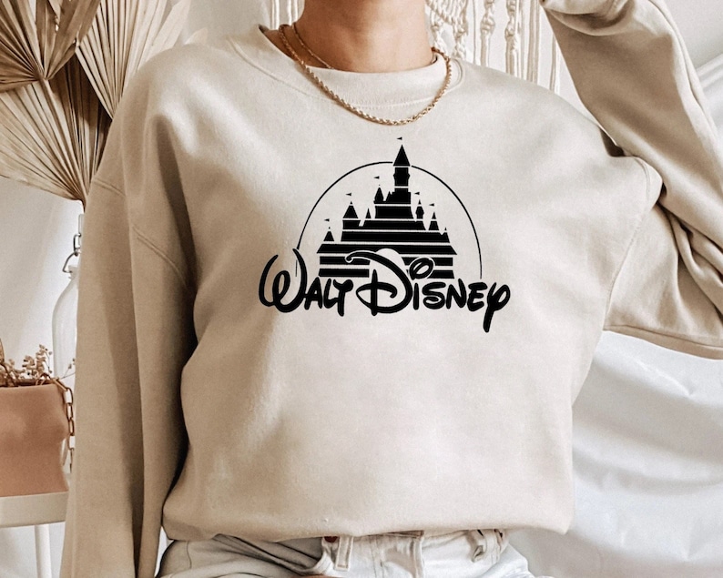 May include: A beige sweatshirt with a black graphic of the Walt Disney World castle and the text "Walt Disney" in a stylized font.