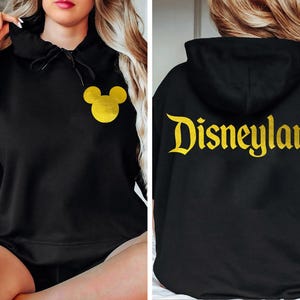 May include: Black hoodie with a gold Mickey Mouse head on the front and the word "Disneyland" in gold on the back.
