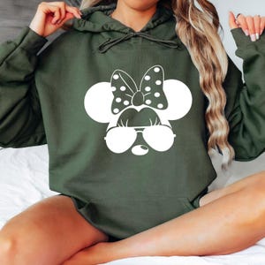 May include: A green hooded sweatshirt with a white graphic of a cartoon mouse wearing sunglasses and a bow. The mouse has large ears and a polka dot bow.