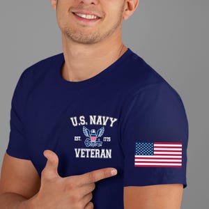 May include: Navy blue t-shirt featuring the text "U.S. NAVY VETERAN" with an eagle emblem and the American flag on the sleeve. The shirt is a classic crew neck style.