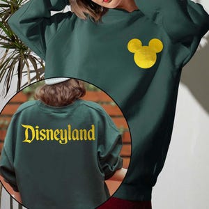 Forest Green Disneyland Sweatshirt With Gold Letter featuring a Minnie Mouse design on the front and Disneyland text on the back, perfect for Disney fans. This cozy Disney Crewneck is great for trips or casual wear.