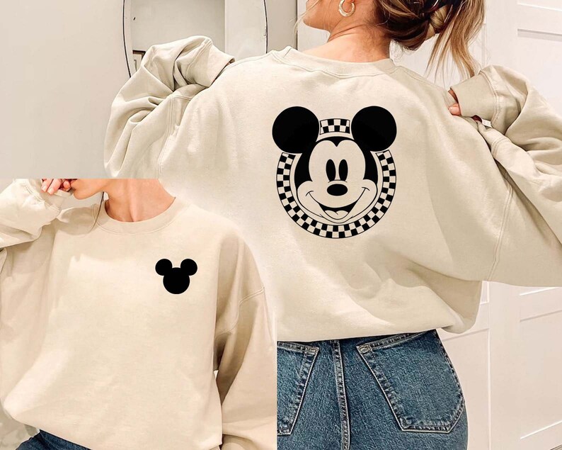 May include: Two cream-colored sweatshirts with black Mickey Mouse designs. One sweatshirt has a large Mickey Mouse head with a checkered border on the back. The other sweatshirt has a small Mickey Mouse head on the front.