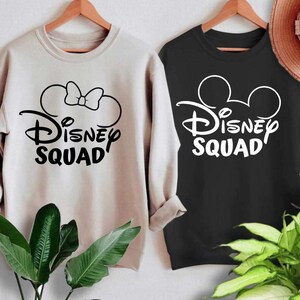 Puede incluir: Dos sudaderas con un gr&aacute;fico de Disney Squad. Una sudadera es beige con un gr&aacute;fico negro de orejas de Minnie Mouse y un lazo. La otra sudadera es negra con un gr&aacute;fico blanco de orejas de Mickey Mouse.