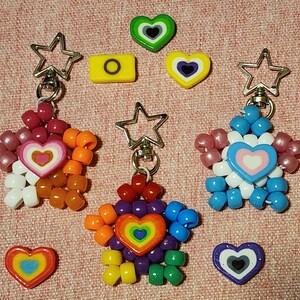 May include: Keychains with star-shaped charms made of colorful beads. Each keychain features a different heart design in the center. Additional heart-shaped and rectangular charms are scattered around the keychains.
