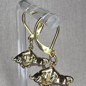 May include: A pair of gold-toned leverback earrings featuring a three-dimensional bull charm. Each earring displays a polished, metallic bull figure suspended from a secure hinged leverback closure, showcasing detailed horns and muscular body contours.