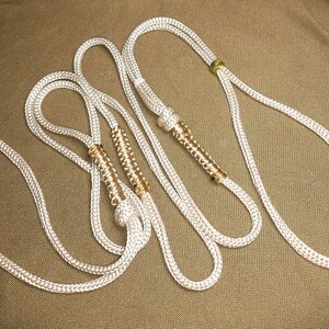 May include: Three white rope lanyards with gold accents. The lanyards are twisted together and have a decorative braided design.