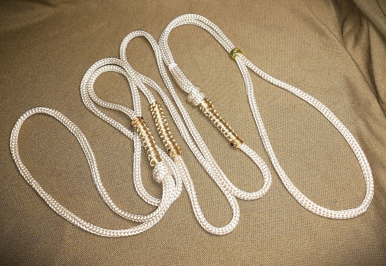 May include: Three white rope lanyards with gold accents. The lanyards are twisted together and have a decorative braided design.