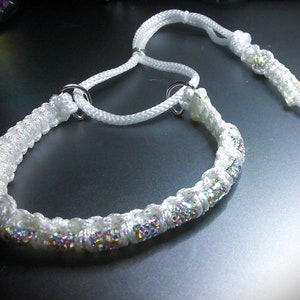 May include: A white, braided dog collar with iridescent glitter accents. The collar features two silver metal rings and a matching leash. The design is simple yet elegant, suitable for pets.
