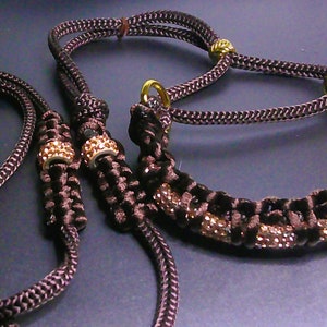 May include: Brown and black dog collar and leash set. The collar and leash are made of braided rope with gold-colored metal accents and sparkling embellishments. The set is designed for pets.