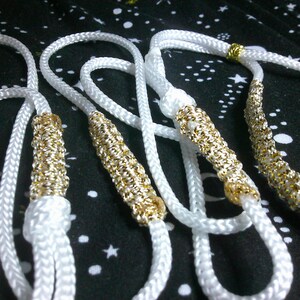 May include: Four white rope necklaces with gold accents. The necklaces are braided and have a decorative gold trim.