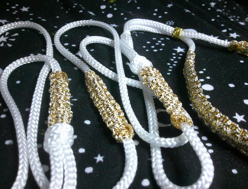May include: Four white rope necklaces with gold accents. The necklaces are braided and have a decorative gold trim.